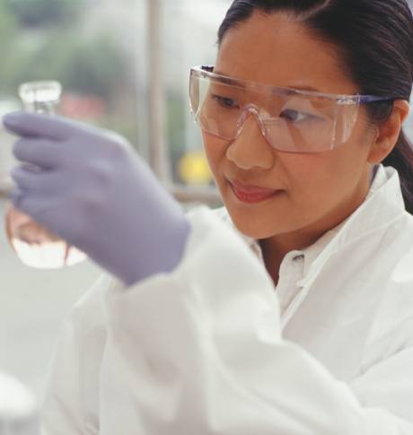 穿著實驗室保護裝備的女性科學家正在觀察瓶子